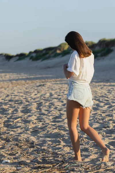 Mujer joven en pantalones cortos de mezclilla caminando en la playa - foto de stock