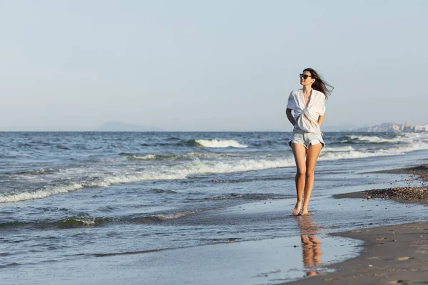 Junge Frau mit Sonnenbrille läuft auf nassem Sand am Strand — Stockfoto