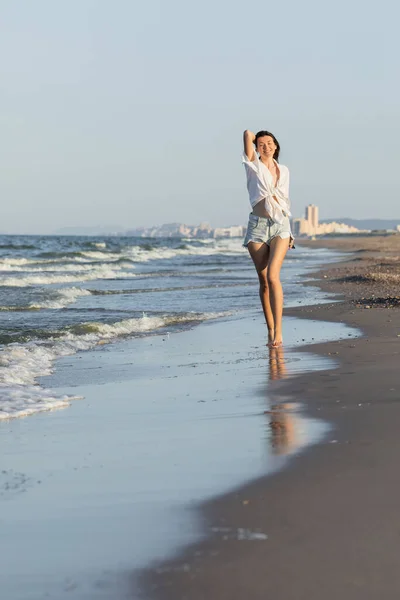 Jolie jeune femme en chemise et jean près de la mer sur la plage — Photo de stock