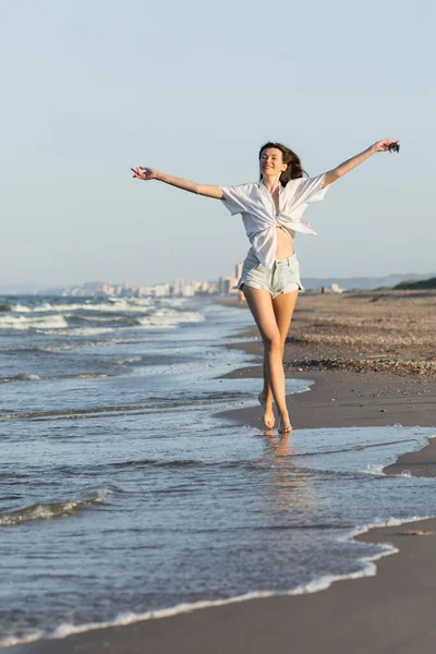 Mulher feliz em shorts e camisa andando perto do mar na praia — Fotografia de Stock