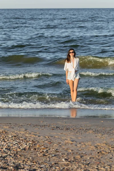 Young woman in sunglasses standing in sea water near beach — Stock Photo