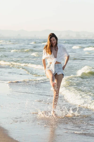 Mujer positiva en camisa blanca arrojando agua al mar - foto de stock