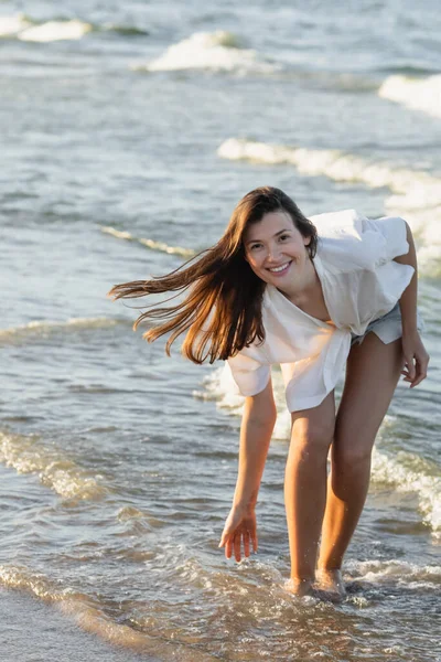 Mujer joven positiva en camisa mirando a la cámara en el mar - foto de stock