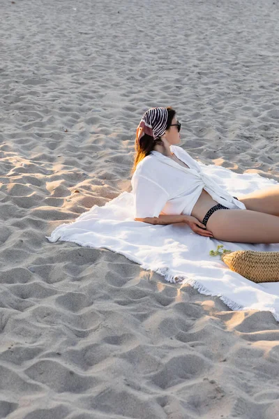 Side view of young woman in swimsuit and shirt lying on handbag on beach — Stock Photo