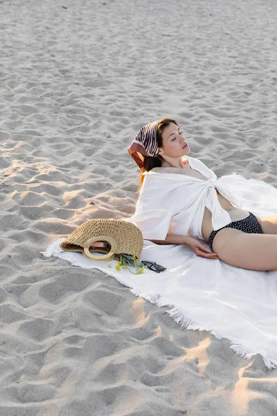 Femme en maillot de bain et chemise reposant près du sac à main et des lunettes de soleil sur la plage — Photo de stock