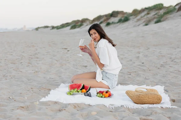 Donna bruna che tiene moglie vicino a frutta fresca e occhiali da sole sulla spiaggia — Foto stock