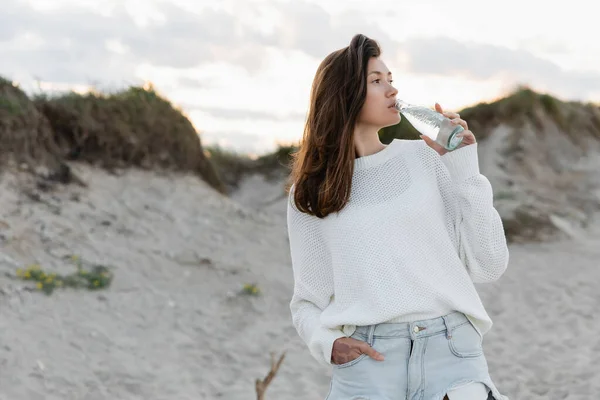 Junge Frau trinkt am Abend Wasser am verschwommenen Strand — Stockfoto