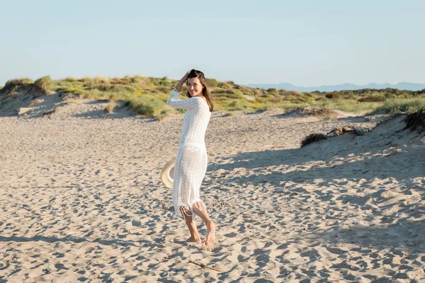 Улыбающаяся женщина в платье, держащая шляпу на пляже днем — стоковое фото