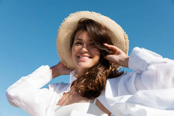 Low angle view of happy young woman in swimsuit and white shirt wearing straw hat against blue sky — Stock Photo