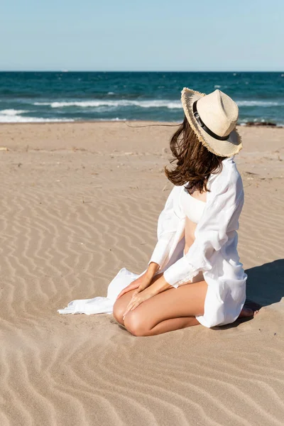 Молода жінка в солом'яному капелюсі сидить на золотому піску біля океану — стокове фото