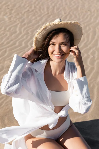 Vista de alto ângulo da jovem mulher em camisa branca e roupa de banho usando chapéu de palha na praia — Fotografia de Stock