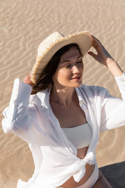 High angle view of young woman in white shirt and swimwear wearing sun hat on beach — Stock Photo