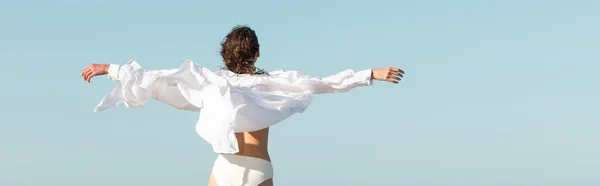 Visão traseira da jovem mulher em camisa branca e roupa de banho de pé com as mãos estendidas, banner — Fotografia de Stock