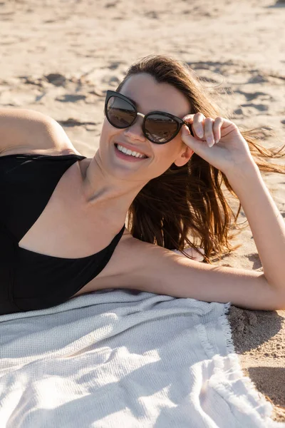 Mujer joven feliz en gafas de sol con estilo acostado en la manta en la playa de arena - foto de stock