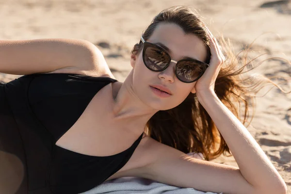 Молодая женщина в стильных солнцезащитных очках лежит на одеяле на песчаном пляже — стоковое фото