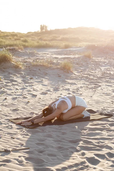 Donna sportiva in sneakers bianche che si esercita sul tappeto fitness sulla spiaggia sabbiosa — Foto stock