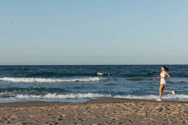 Piena lunghezza di giovane donna sportiva jogging vicino al mare in estate — Foto stock