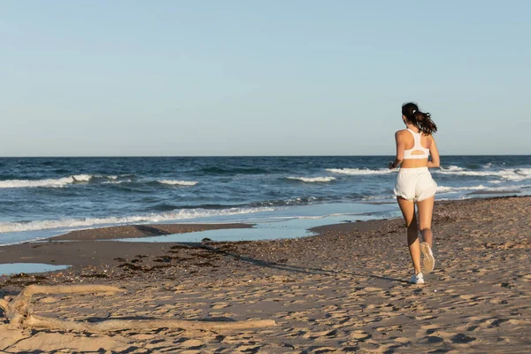 Вид сзади на молодую спортивную женщину, бегущую летом у моря — стоковое фото