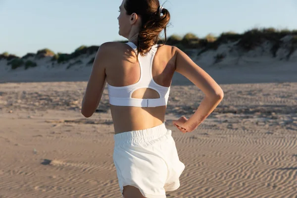 Junge brünette Frau in weißer Sportbekleidung joggt im Sommer am Strand — Stockfoto
