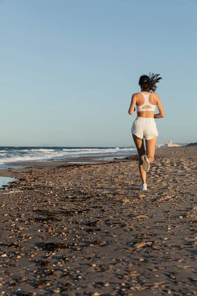 Вид сзади на спортивную женщину в белых шортах, бегущую летом у моря — стоковое фото