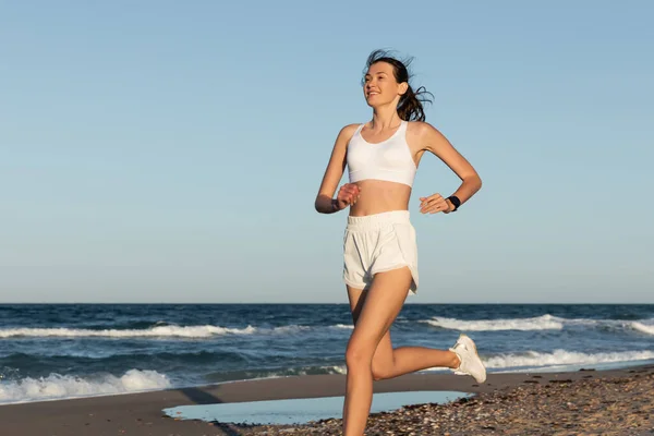 Sorridente giovane donna in abbigliamento sportivo fare jogging vicino al mare in estate — Foto stock