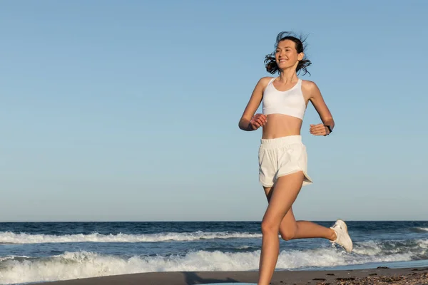 Cheerful young and sportive woman jogging near sea in summer — Stock Photo