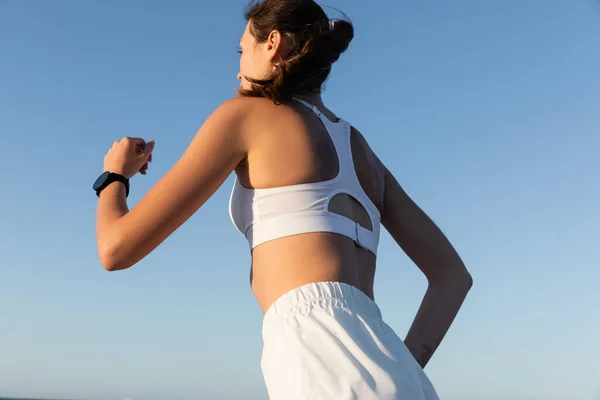 Vista de ángulo bajo de la mujer joven y deportiva corriendo contra el cielo azul en verano - foto de stock