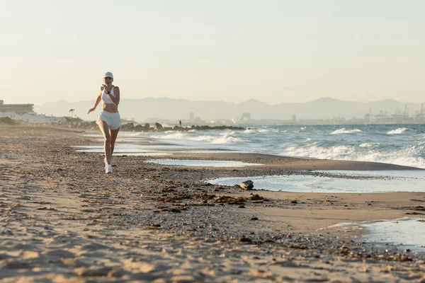 Брюнетка спортивная женщина в бейсболке бег трусцой около моря летом — стоковое фото