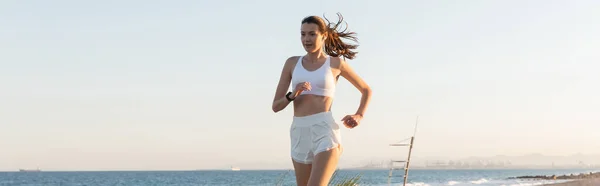 Junge Frau in kurzen Hosen und drahtlosem Kopfhörerjogging in der Nähe des Meeres, Banner — Stockfoto