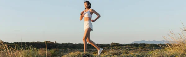 Mujer en pantalones cortos y sujetador deportivo escuchar música y correr fuera, pancarta - foto de stock