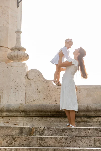 Mãe sorridente em vestido segurando filha em escadas de pedra da ponte Puente Del Mar em Valência — Fotografia de Stock