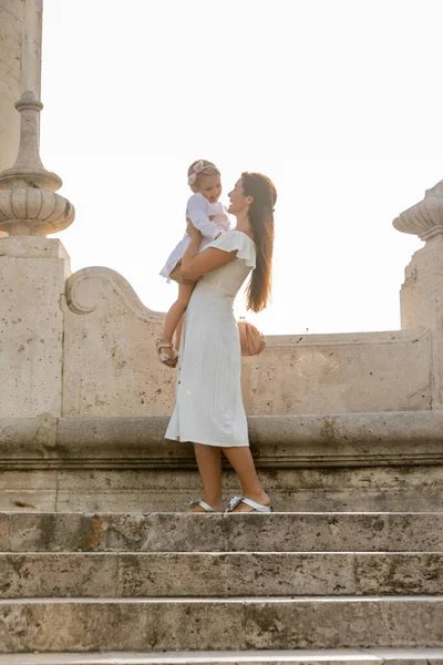 Fröhliche Frau hält Kleinkind-Tochter auf Steintreppe der Brücke Puente del Mar in Valencia — Stockfoto
