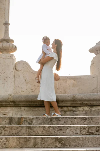 Cheerful woman holding toddler daughter on stone stairs of Puente Del Mar bridge in Valencia — Stock Photo