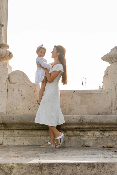 Brunette woman holding smiling daughter near stone Puente Del Mar bridge in Valencia — Fotografia de Stock