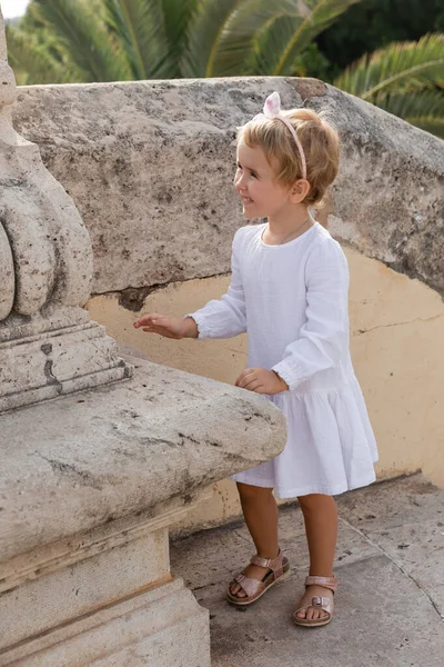 Smiling baby girl in dress standing near stone Puente Del Mar bridge in Valencia — Photo de stock