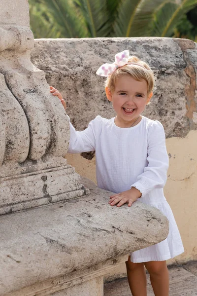 Positive toddler child in summer dress looking at camera near stone Puente Del Mar bridge in Valencia — Photo de stock