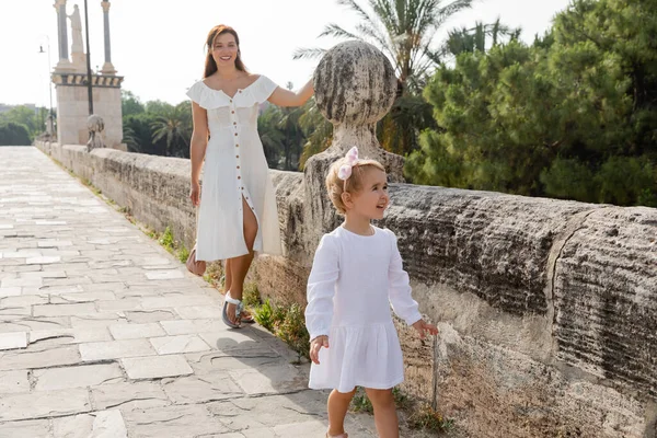 Toddler child in dress looking away near mom on Puente Del Mar bridge in Valencia — Photo de stock