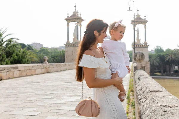 Smiling parent holding baby daughter on Puente Del Mar bridge in Valencia - foto de stock