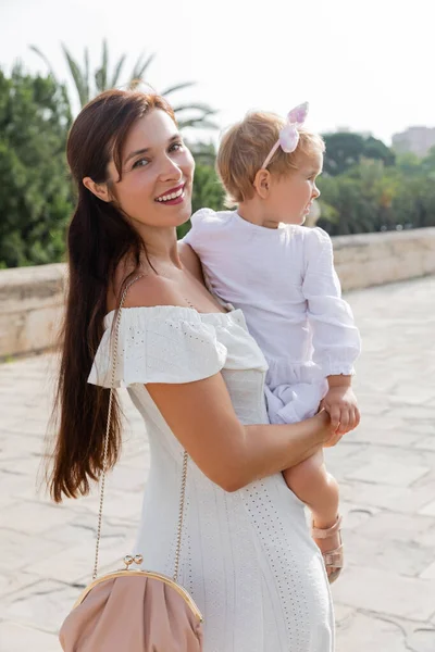 Madre positiva in abito guardando la fotocamera mentre tiene il bambino sul ponte Puente Del Mar a Valencia — Foto stock