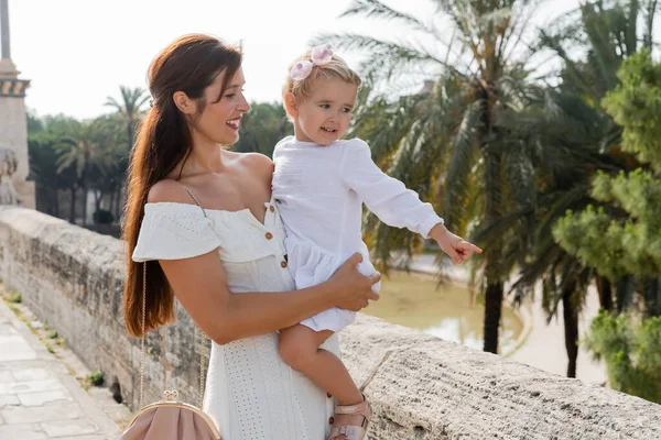 Madre positiva mirando a la pequeña hija señalando con el dedo el puente Puente Del Mar en Valencia - foto de stock