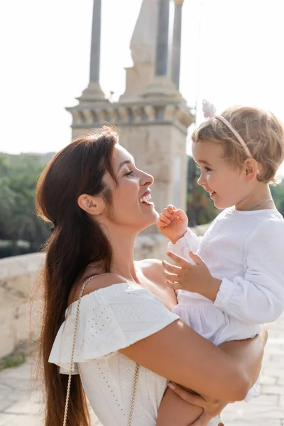 Seitenansicht einer glücklichen brünetten Mutter, die ihre kleine Tochter in Valencia umarmt — Stockfoto