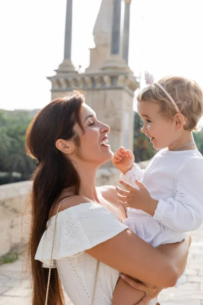 Vista laterale della felice mamma bruna che abbraccia la bambina a Valencia — Foto stock