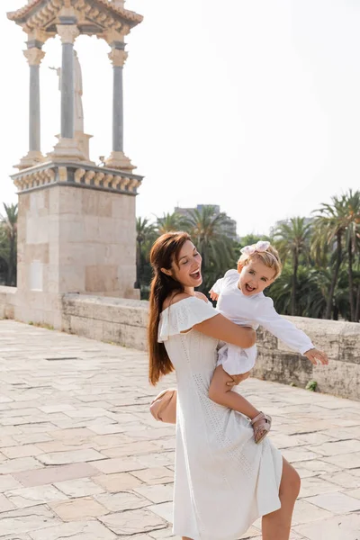 Excited mom embracing baby girl in summer dress on Puente Del Mar bridge in Valencia — Stock Photo