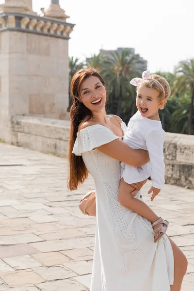 Bruna donna guardando la fotocamera mentre abbraccia il bambino sul ponte Puente Del Mar a Valencia — Foto stock