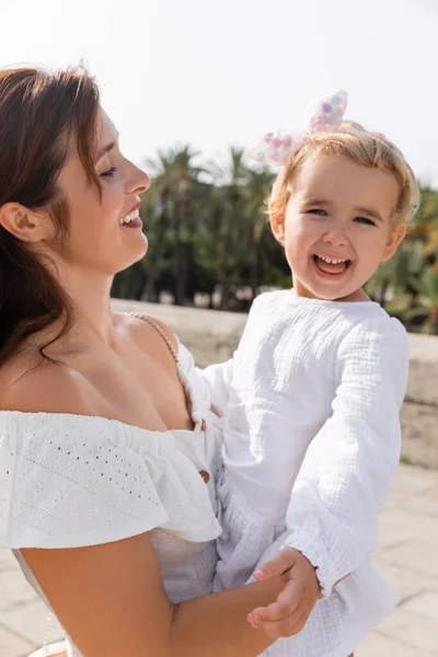 Portrait of baby girl in white dress looking at camera near mom in Valencia — Photo de stock