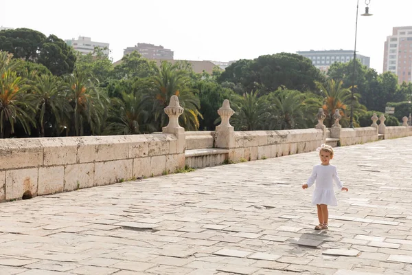 Smiling toddler girl in white summer dress walking on Puente Del Mar bridge in Valencia — Stock Photo