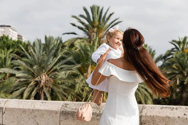 Женщина играет с улыбающимся ребенком возле пальм на заднем плане в Валенсии — стоковое фото