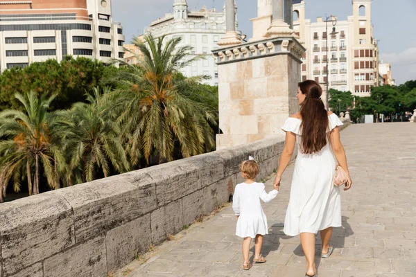 Woman in white dress holding hand of kid while walking on Puente Del Mar bridge in Valencia — Photo de stock