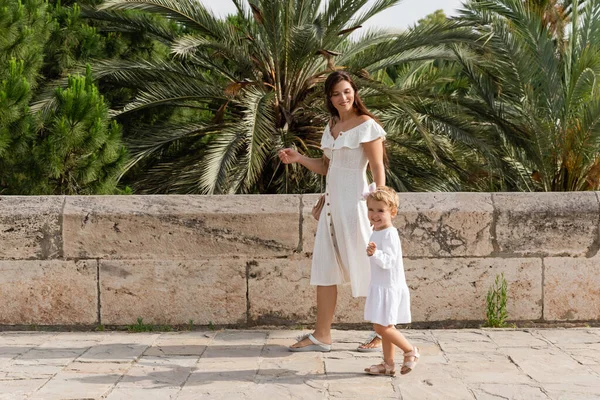 Niño positivo mirando a la cámara mientras camina cerca de mamá en Valencia - foto de stock