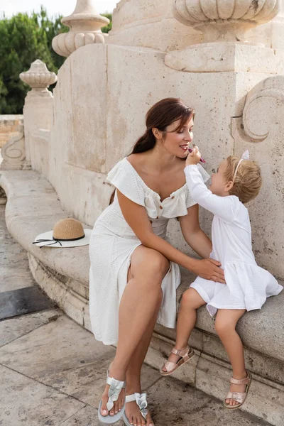 Petite fille appliquant du brillant à lèvres sur les lèvres mères sur le banc de pierre du pont Puente Del Mar à Valence — Photo de stock